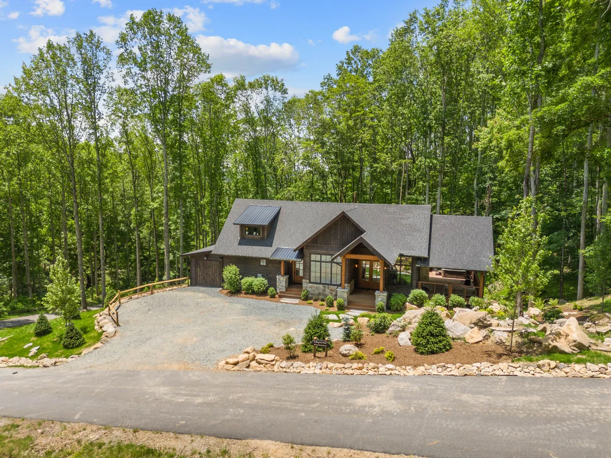 An exterior shot of the main entrance, surrounded by lush greenery and a gravel driveway. The image hints at the cabin's natural setting—inviting guests to begin their outdoor experiences right from the front door.