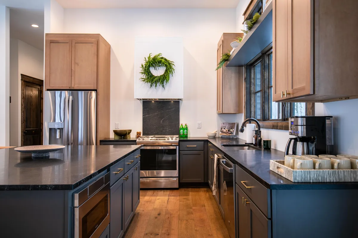 A wide view of the open-concept kitchen, focused on a central island with dark granite countertops, stainless steel appliances, and a decorative wreath above the stove hood. The space is inviting, designed for cooking and socializing, with ample room for gathering.