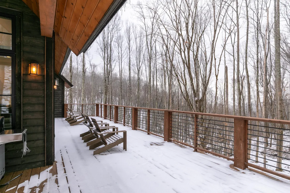 An exterior angle of the home’s snow-covered deck with inviting lounge chairs, bordered by trees and gentle winter light. The deck offers plenty of space for outdoor socializing, relaxing, or simply enjoying the peaceful view as a group.