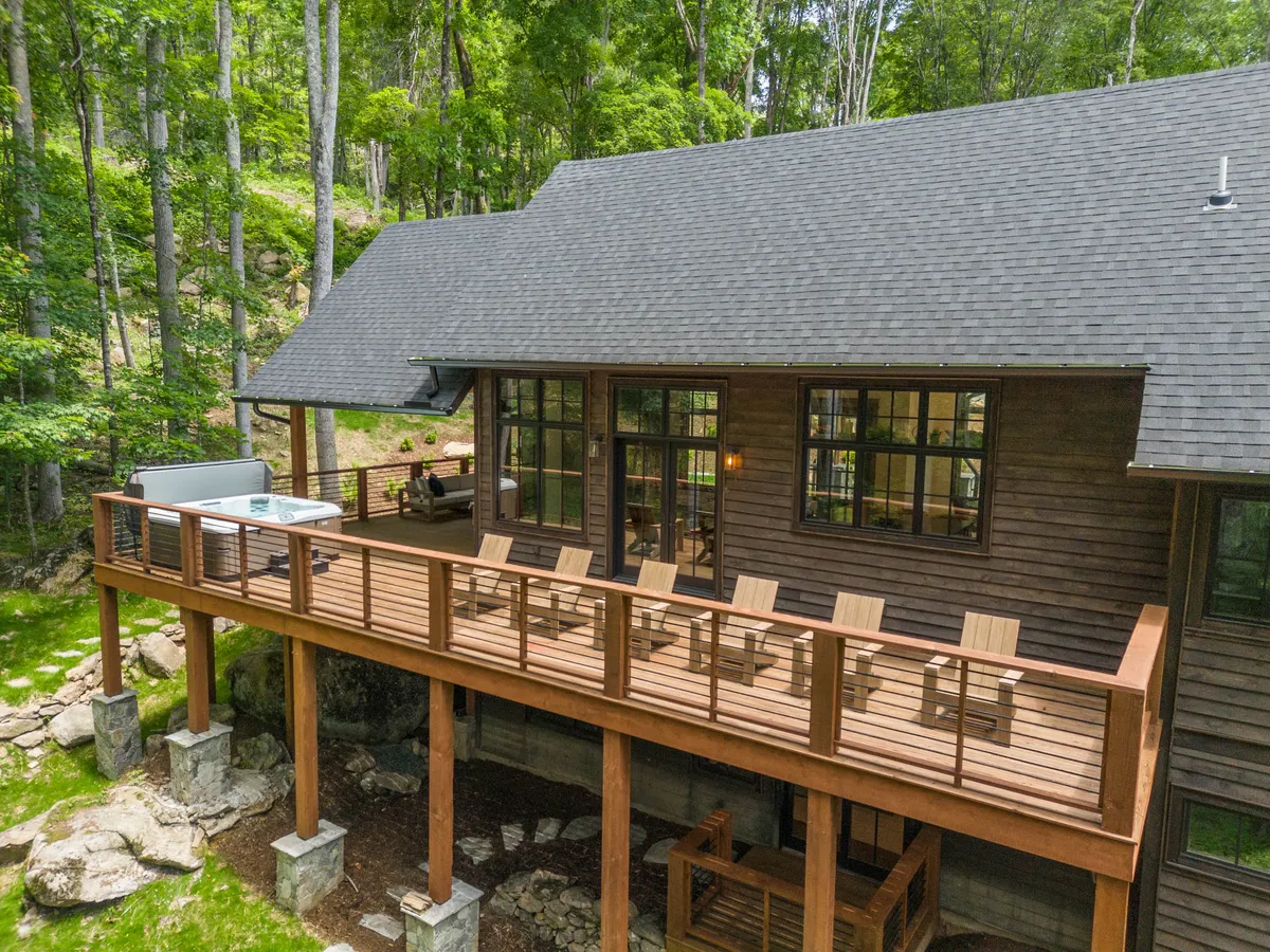 An inviting wooden deck with comfortable seating and a hot tub overlooks a natural landscape. Large windows connect the indoor living space with the outdoors, while the deck is positioned for sunset views or stargazing in the mountain air.