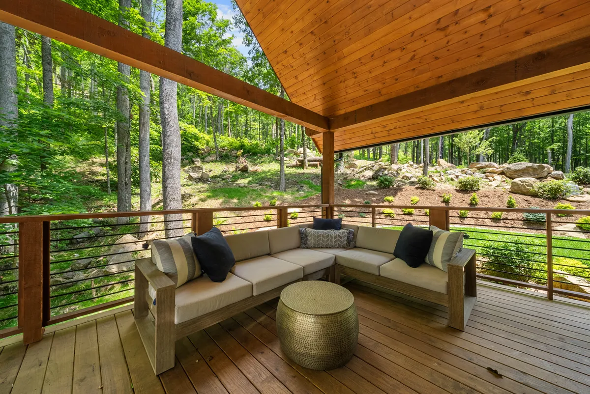 A tranquil wooden deck furnished with sofa seating, decorative cushions, a metallic coffee table, and lush greenery in the background. The space feels open and inviting, ideal for relaxing after a day of outdoor excitement.