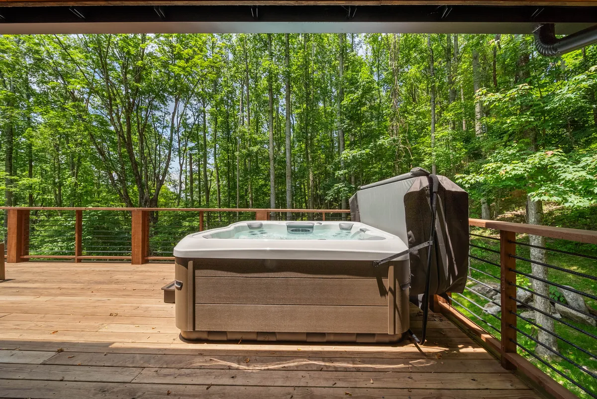 This image features an outdoor hot tub on a wooden deck surrounded by lush greenery. The scene exudes serenity and comfort, inviting guests to relax and take in the natural mountain setting. The hot tub is the focal point, perfect for unwinding while enjoying the fresh air and scenic views.