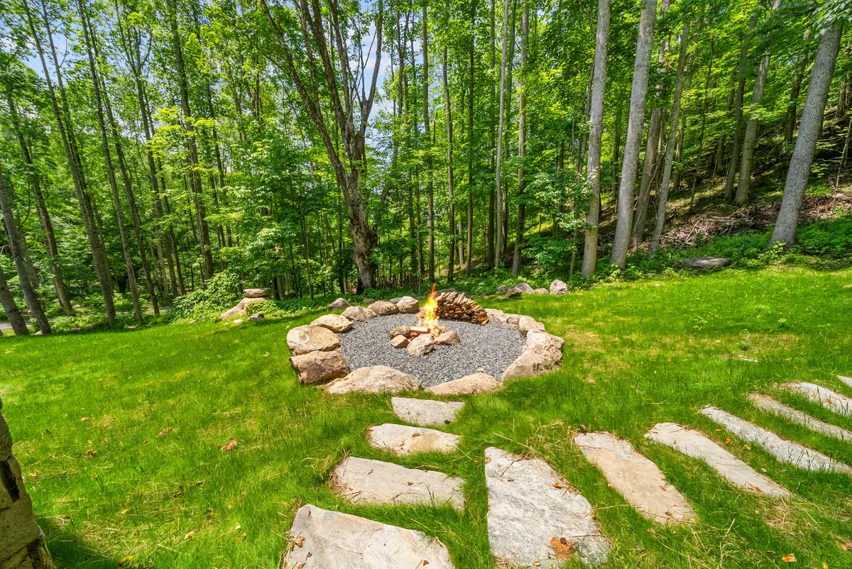 This image captures a welcoming fire pit area surrounded by trees and a stone pathway, inviting families to gather outdoors for campfire activities, storytelling, and stargazing. The lush greenery provides an immersive sense of being in nature, reinforcing the retreat's mountain atmosphere.