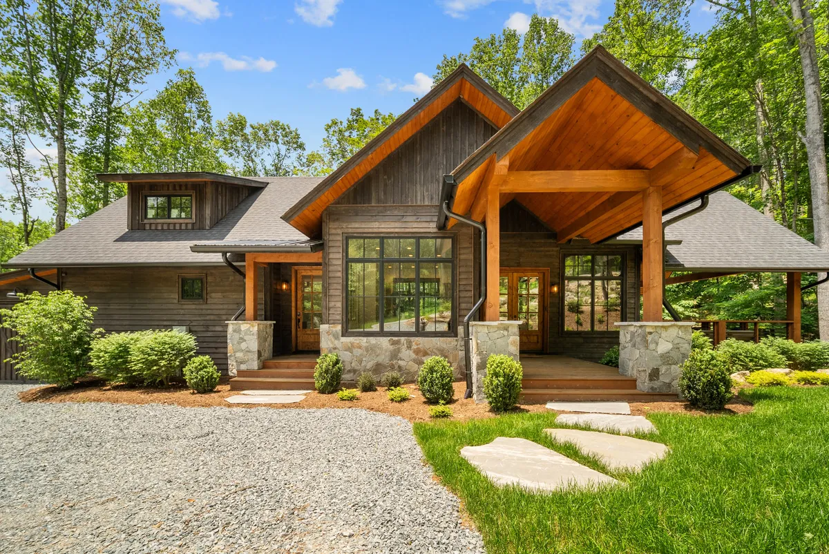 The exterior of the home highlights a welcoming front porch framed by sturdy wooden beams, large windows, and stone accents. The manicured lawn adds to the inviting atmosphere, offering an immediate sense of arrival and setting the scene for both relaxation and outdoor activities.