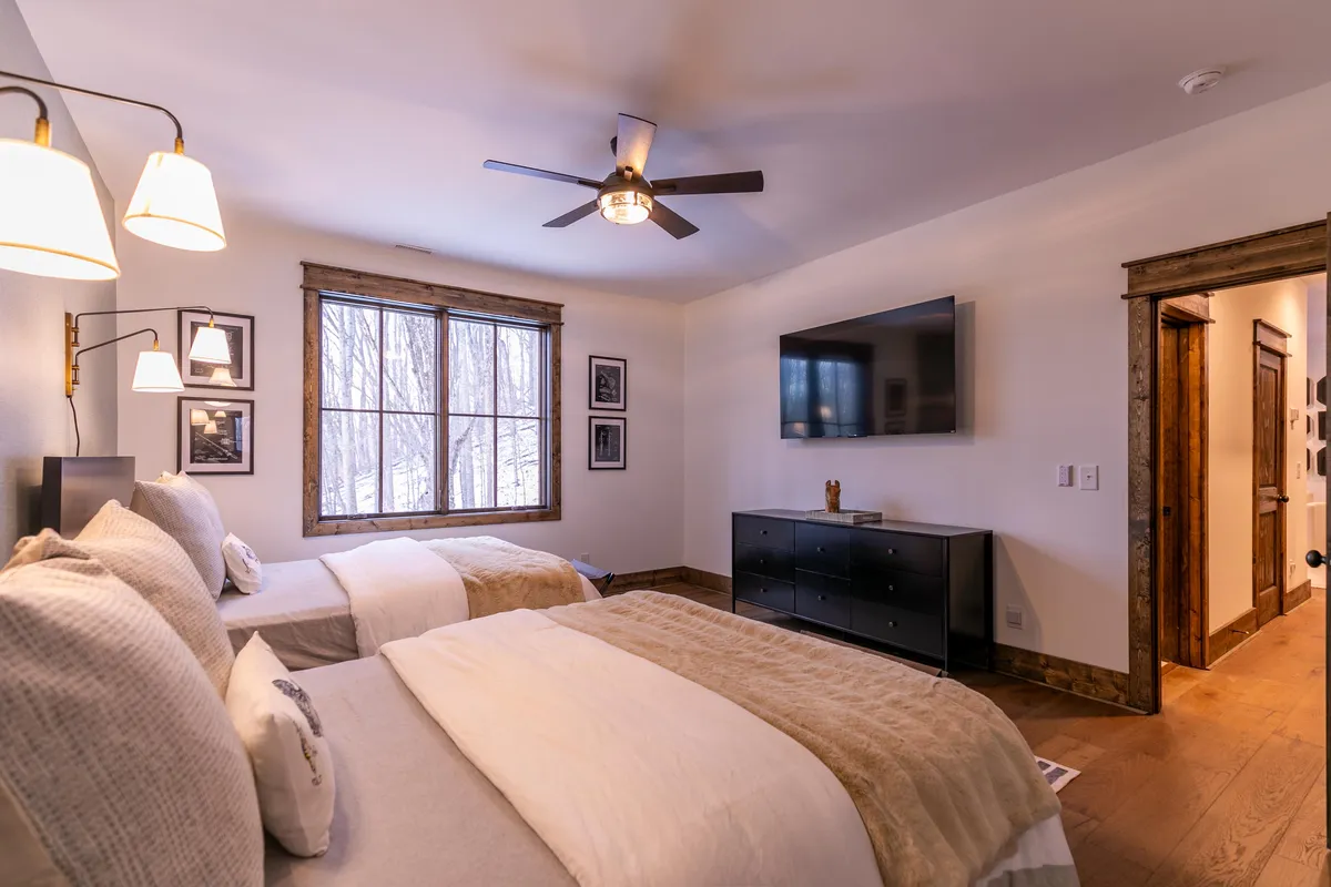 A comfortable bedroom with two beds, a large window offering forest views, a TV, and a dresser with decor. The space feels serene and is perfect for relaxation or unwinding with a movie at the end of the day.
