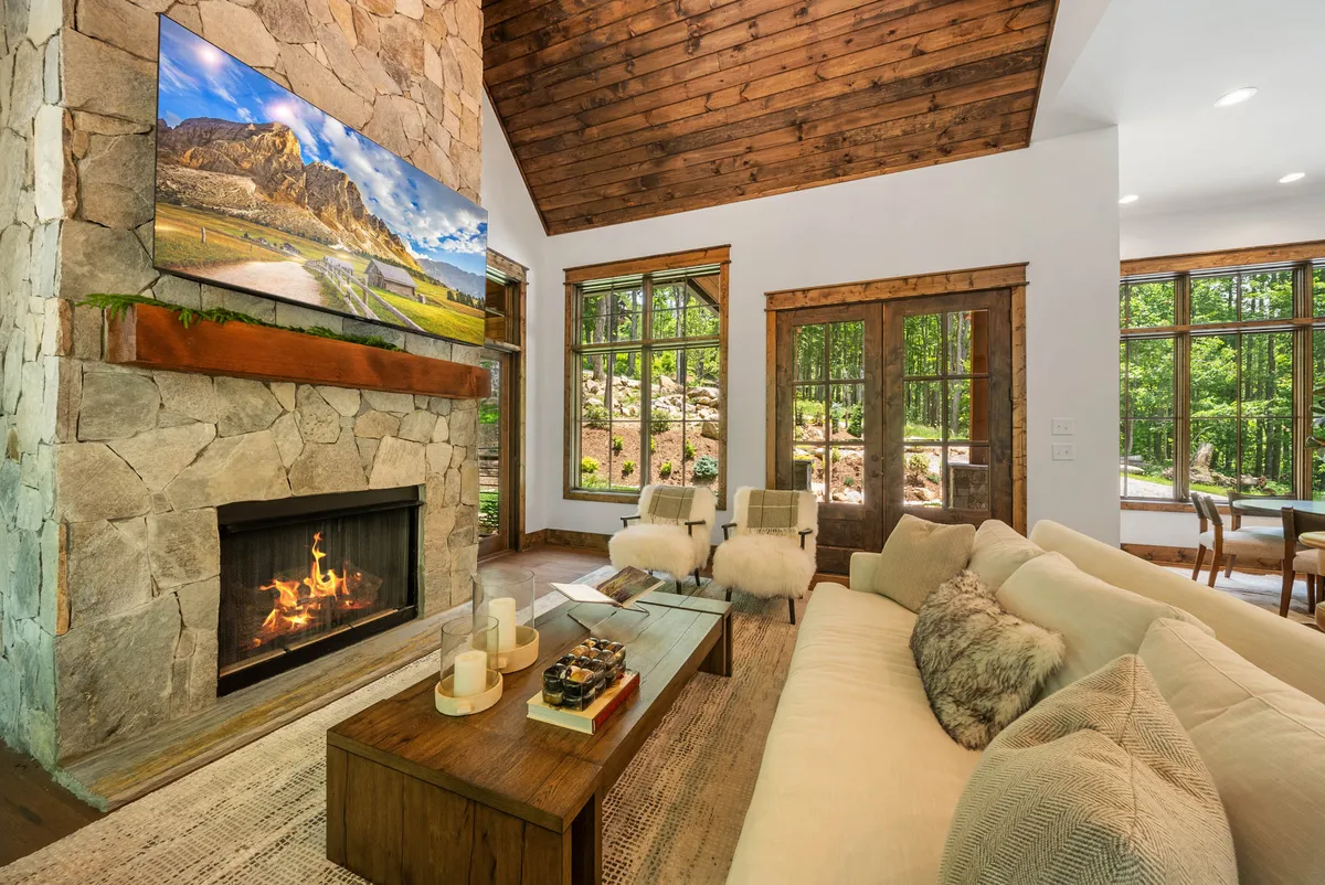 A cozy living room featuring a stone fireplace, large television above the mantle, a comfortable sofa, and a wooden coffee table. Natural light streams in, highlighting the inviting space perfect for movie nights or unwinding by the fire.